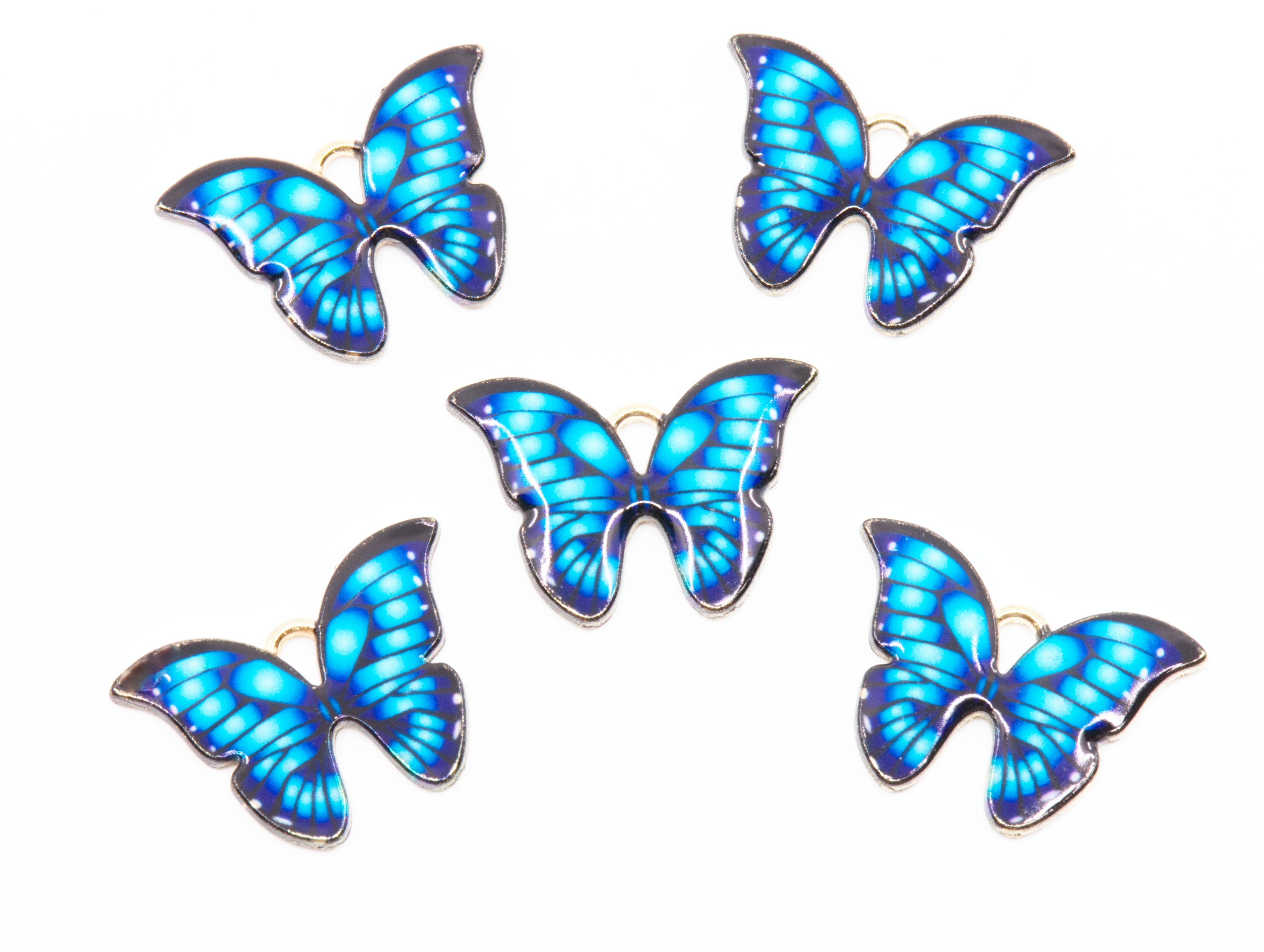 Five butterfly-shaped jewelry charms with vibrant blue and light blue patterned wings and gold-tone metal edges, arranged on a plain white background.