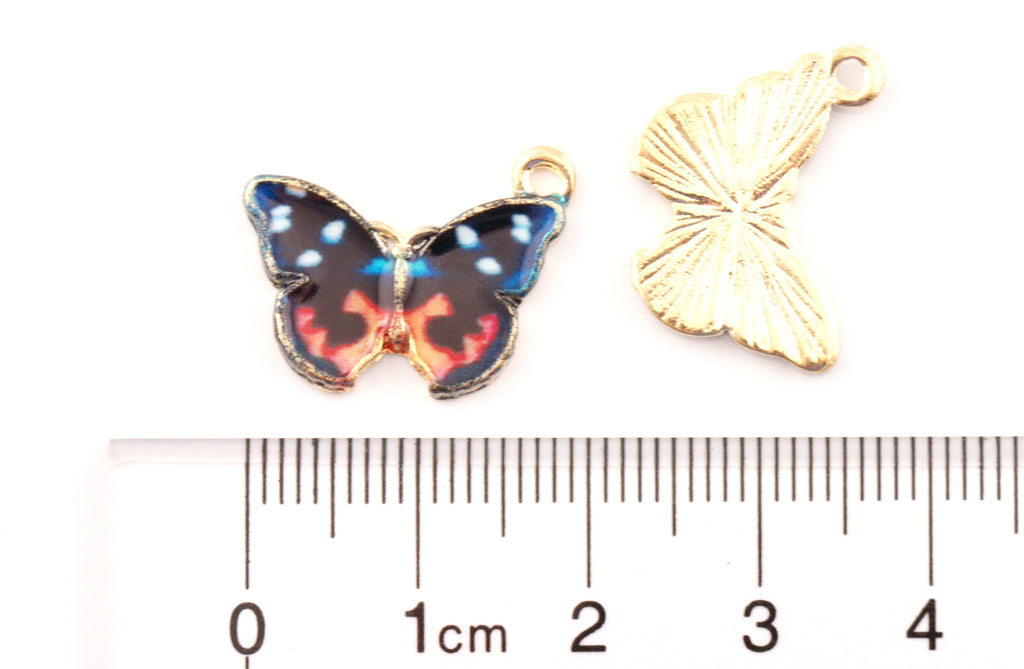 Two butterfly-shaped jewelry charms, orange, and black wings displayed above a cm ruler for scale on a white background.