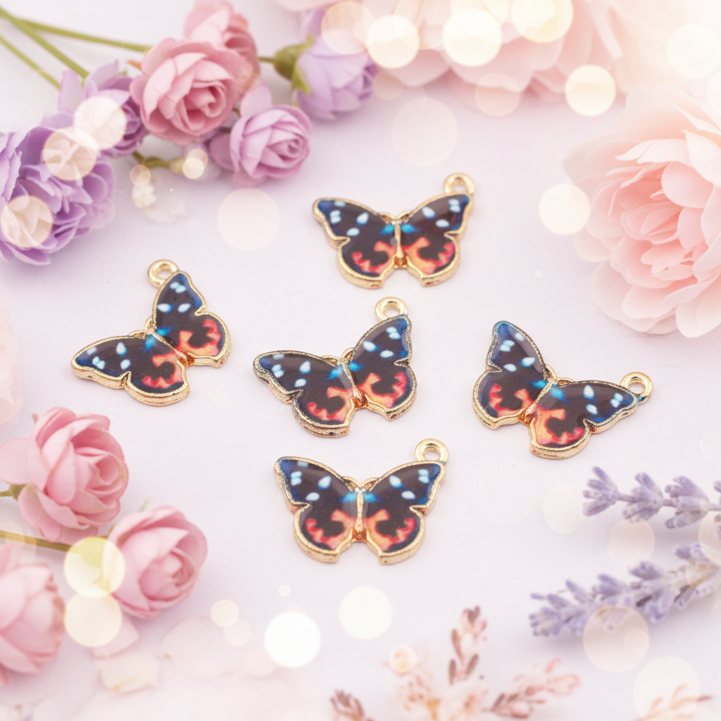 Five butterfly-shaped jewelry charms with gold-tone edges and multicolored patterned wings, arranged on a light pink background with decorative flowers and bokeh lights.