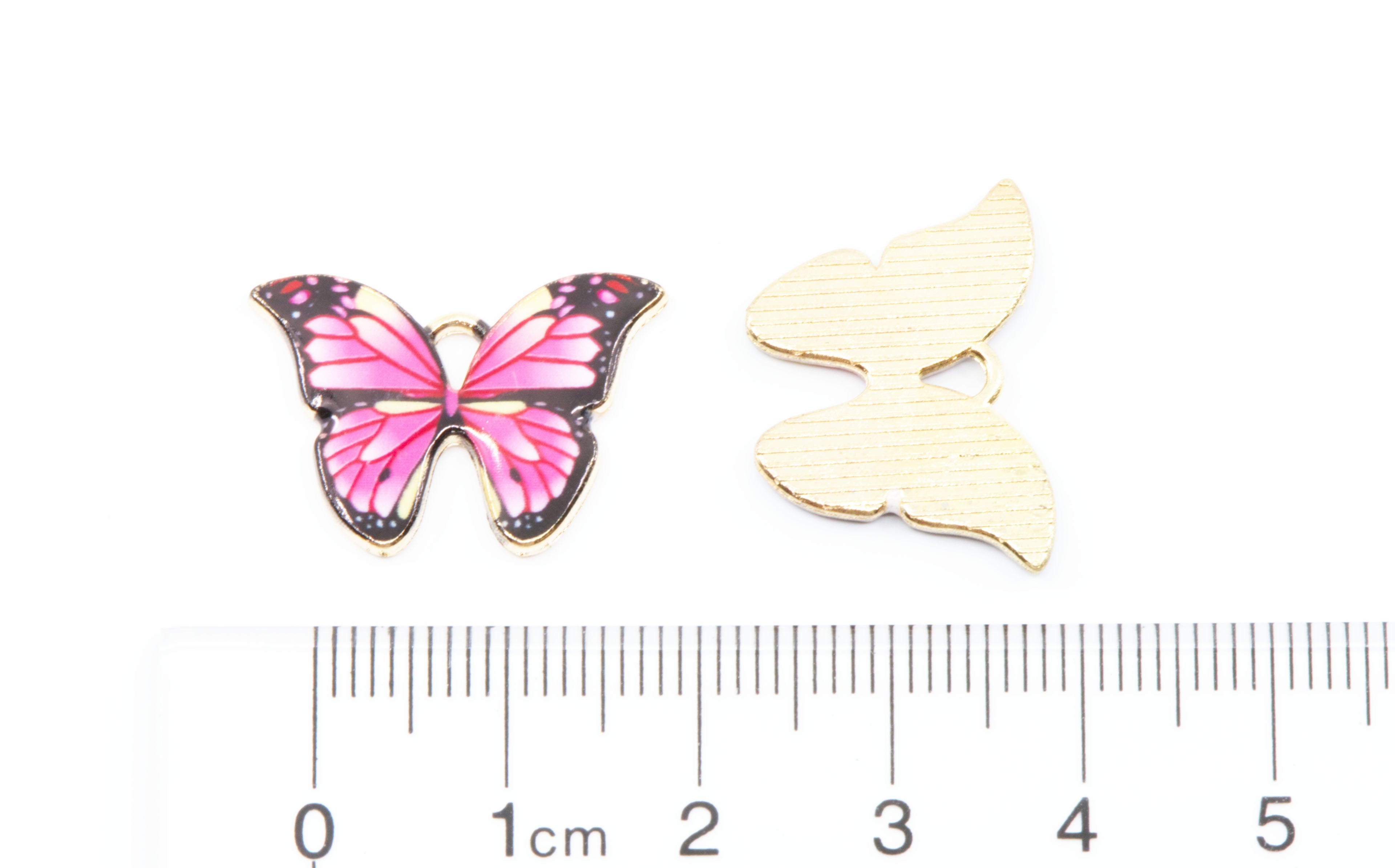 Two butterfly jewelry charms on a white background: cm ruler below for scale.