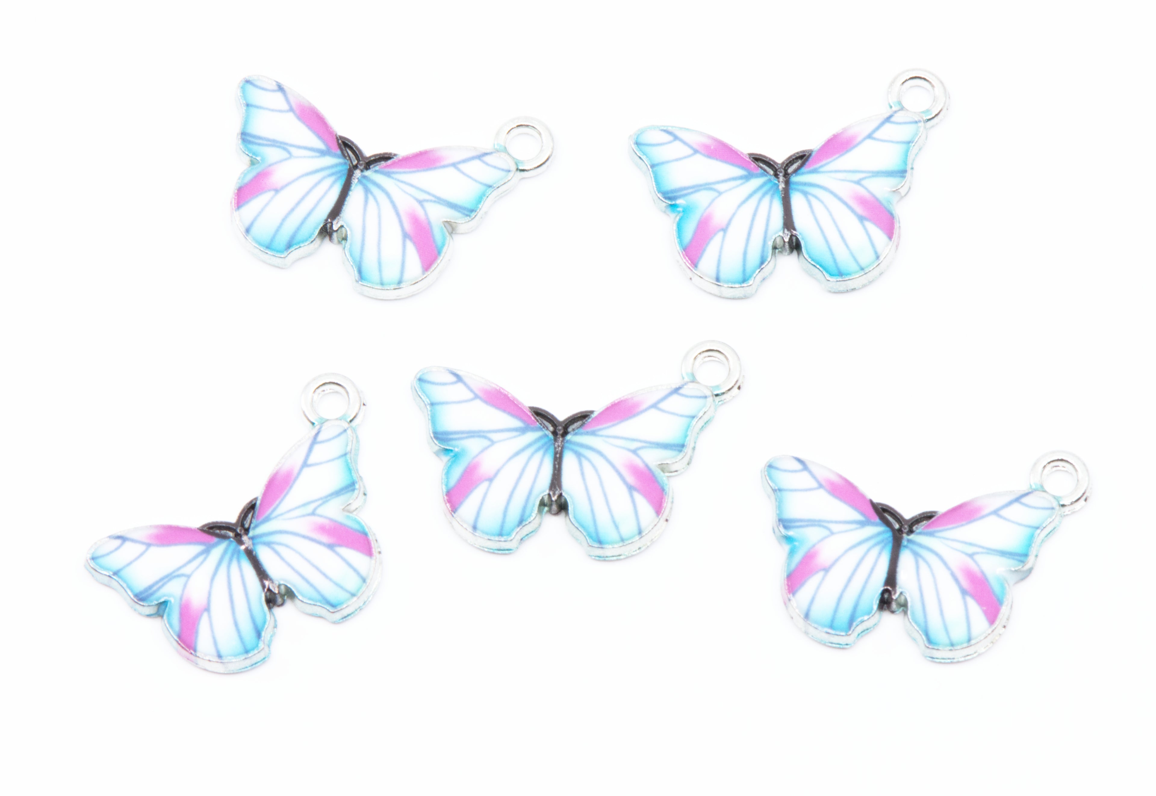 Five butterfly-shaped jewelry charms with silver-toned metal loops, featuring light blue, purple, and white wing patterns on a white background.
