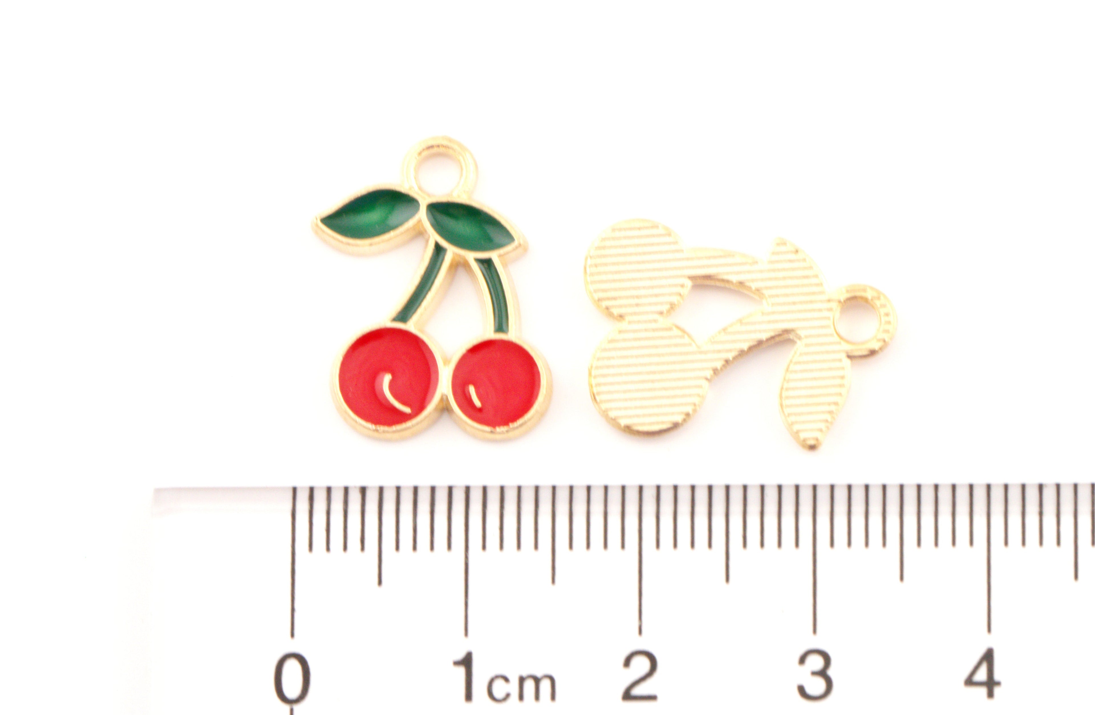Two small red cherry jewelry charms on a white background with a ruler below for scale:  The ruler shows centimeter markings 