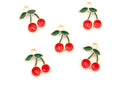 Five cherry-shaped jewelry charms with red enamel, green leaves, and gold-tone metal borders arranged on a plain white background.