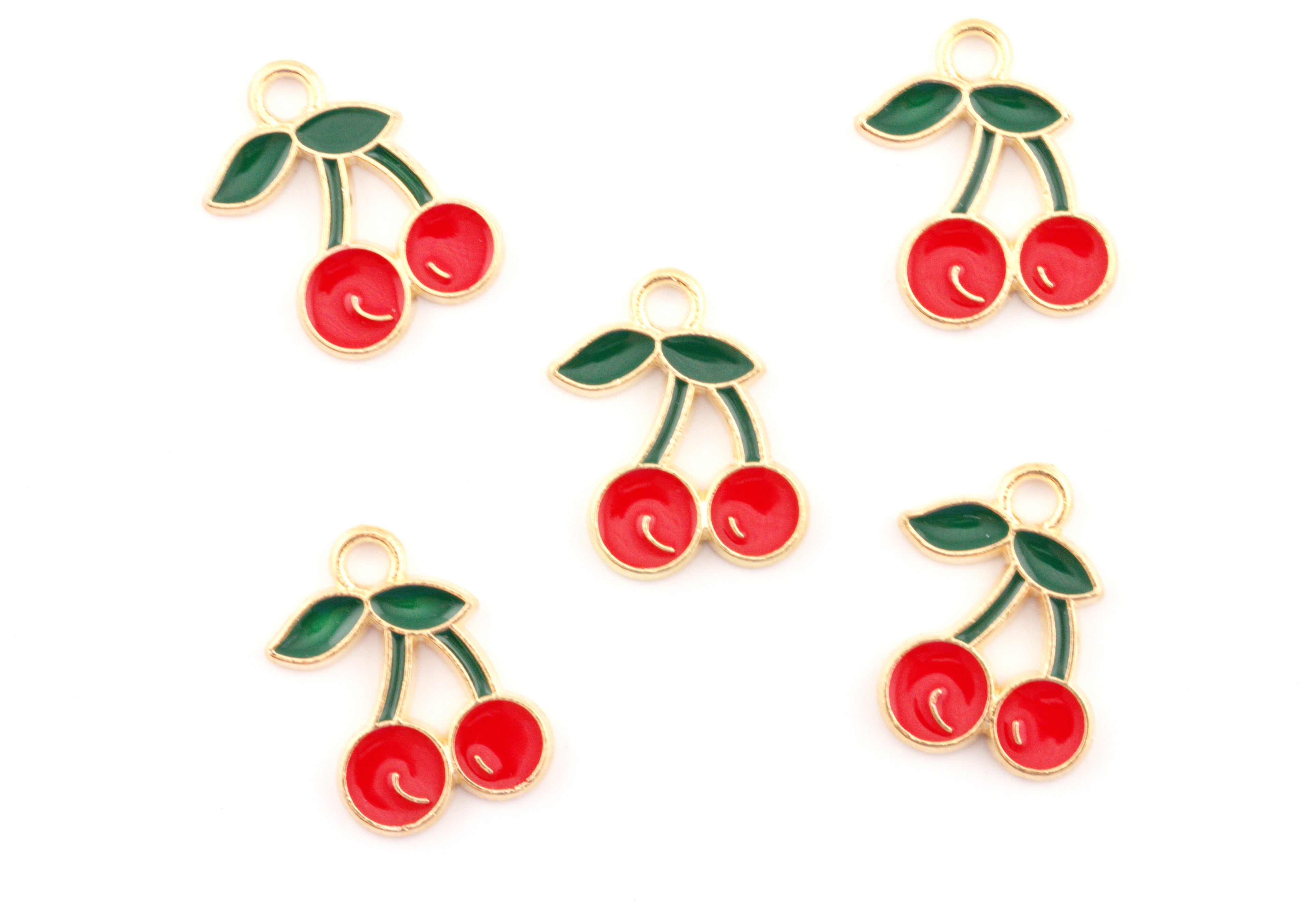 Five cherry-shaped jewelry charms with red enamel, green leaves, and gold-tone metal borders arranged on a plain white background.