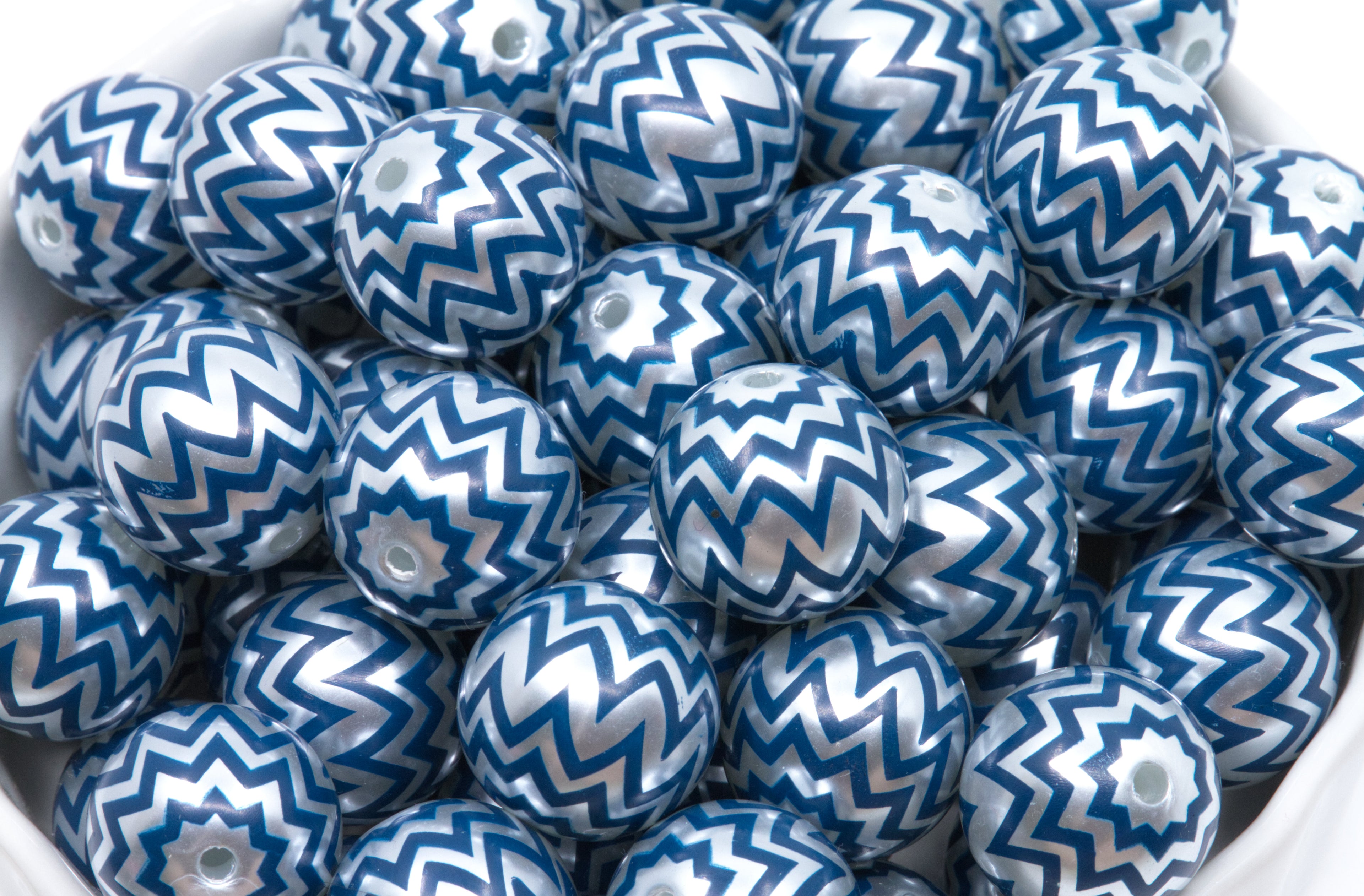 A pile of bubblegum beads with a blue and silver chevron pattern, sitting in a white container.