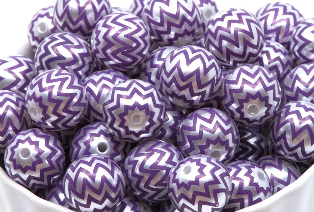 A pile of round craft beads with a purple and silver chevron pattern, shown in a white container.