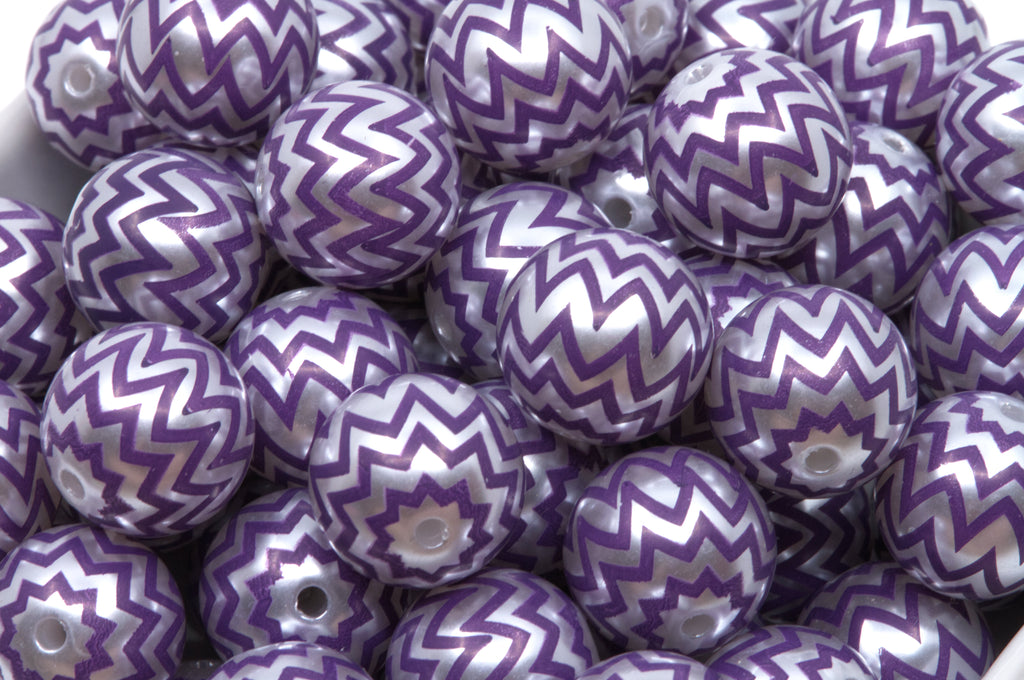 A pile of round craft beads with a purple and silver chevron pattern, shown in a white container.