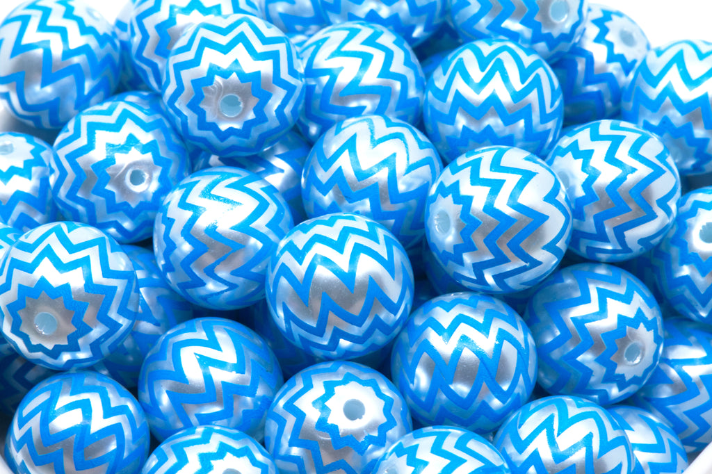 A close-up pile of  blue beads with a silver chevron zigzag pattern in a white bowl. 