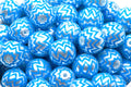 A close-up pile of  blue beads with a silver chevron zigzag pattern in a white bowl. 