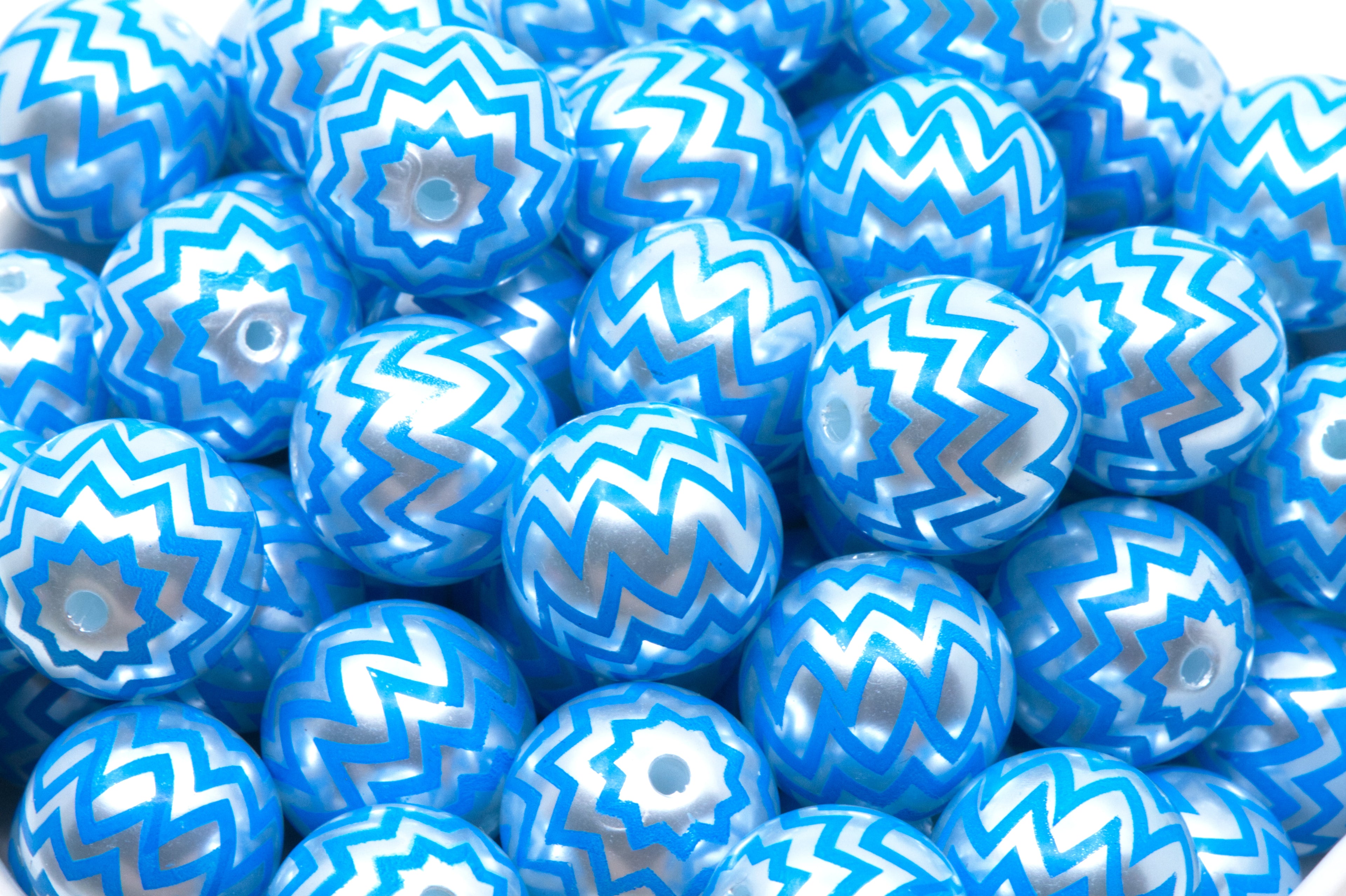 A close-up pile of  blue beads with a silver chevron zigzag pattern in a white bowl. 