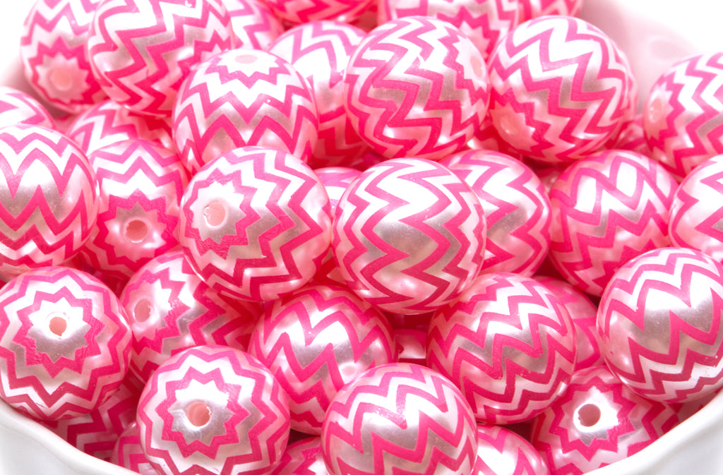 A pile of  pink and silver chevron-patterned round beads in a white container. 