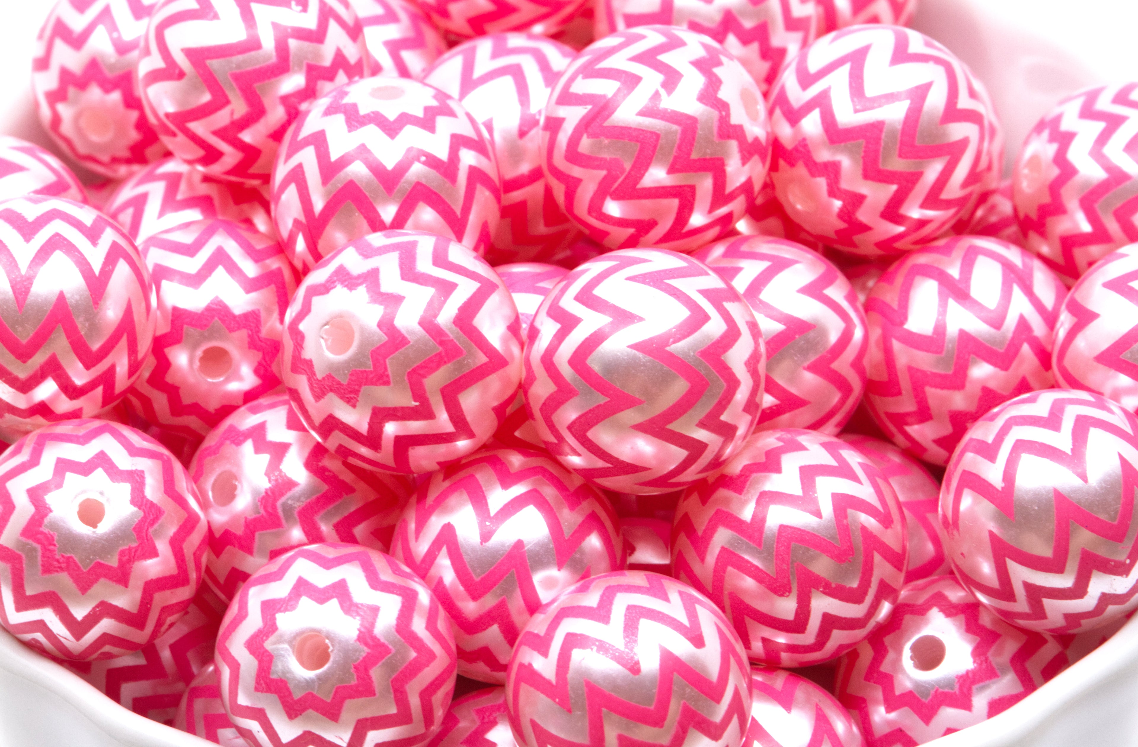 A pile of  pink and silver chevron-patterned round beads in a white container. 