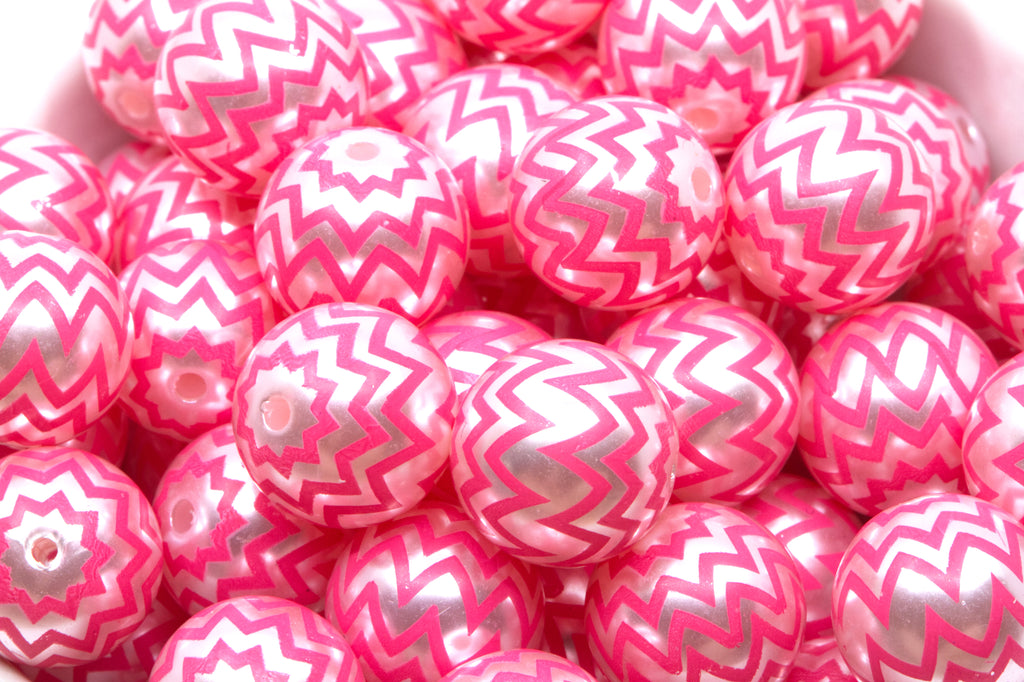 A pile of  pink and silver chevron-patterned round beads in a white container. 