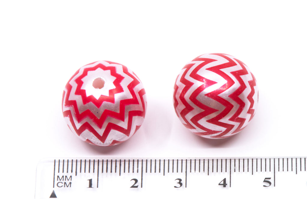 Two round red and silver patterned beads shown next to a cm ruler for scale on a white background.