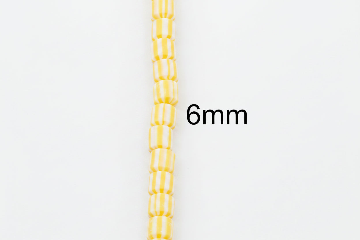 A single strand of small yellow and white striped polymer clay barrel beads shown vertically on a plain white background, with the text '6mm' indicating the bead size. 
