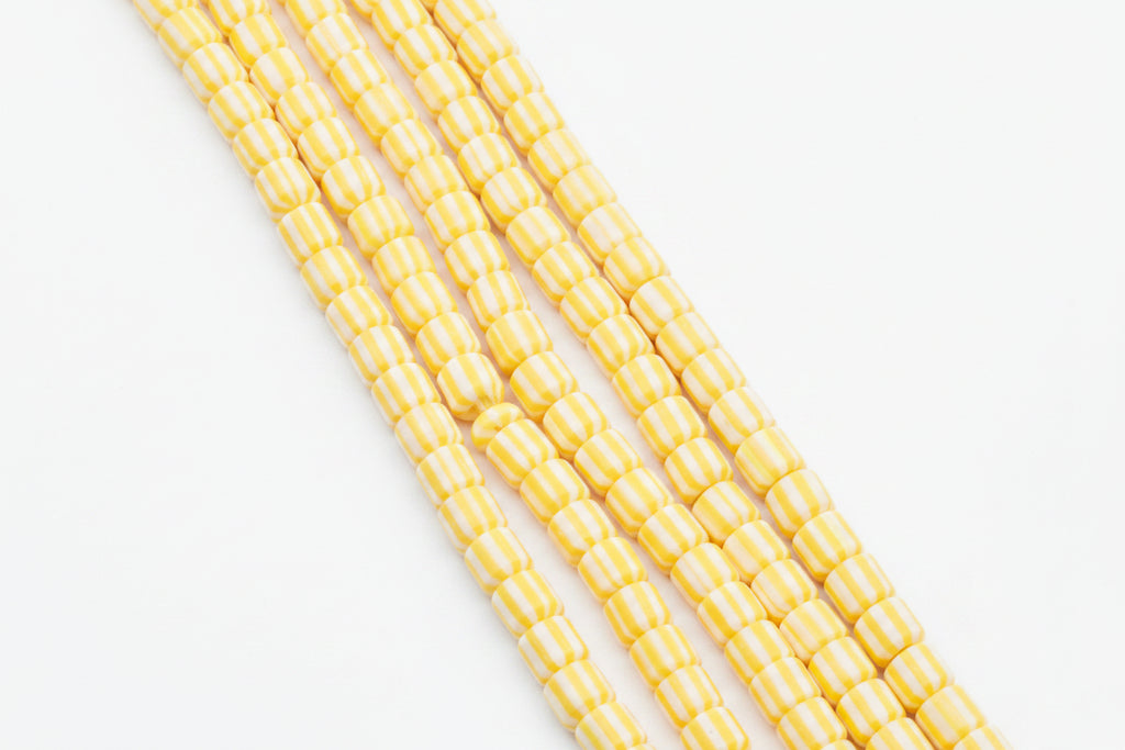 Five strands of polymer clay barrel beads with alternating yellow and white stripes, arranged diagonally on a white background.