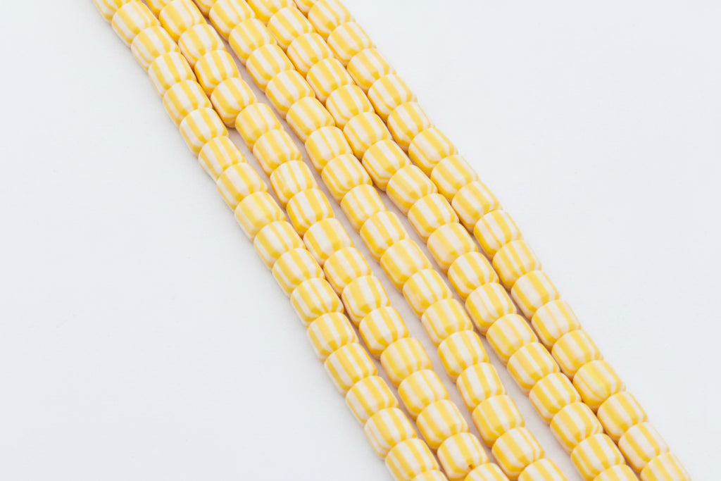 Five strands of polymer clay barrel beads with alternating yellow and white stripes, arranged diagonally on a white background.