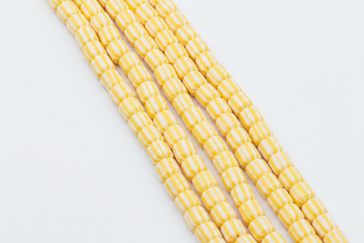 Five strands of polymer clay barrel beads with alternating yellow and white stripes, arranged diagonally on a white background.