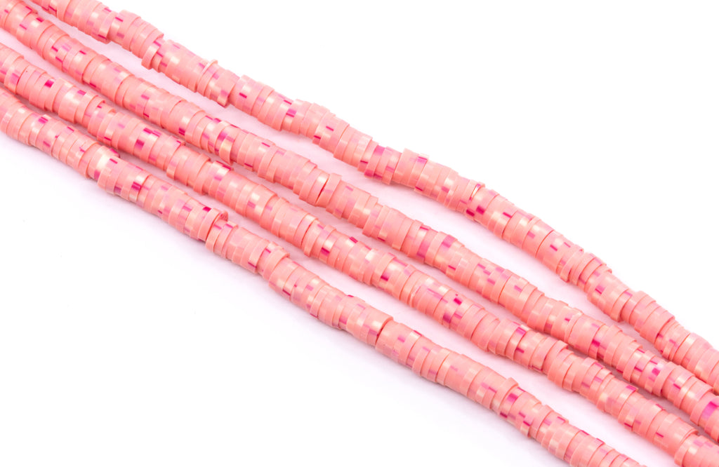 multiple strand of pink polymer clay beads arranged diagonally on a white background.