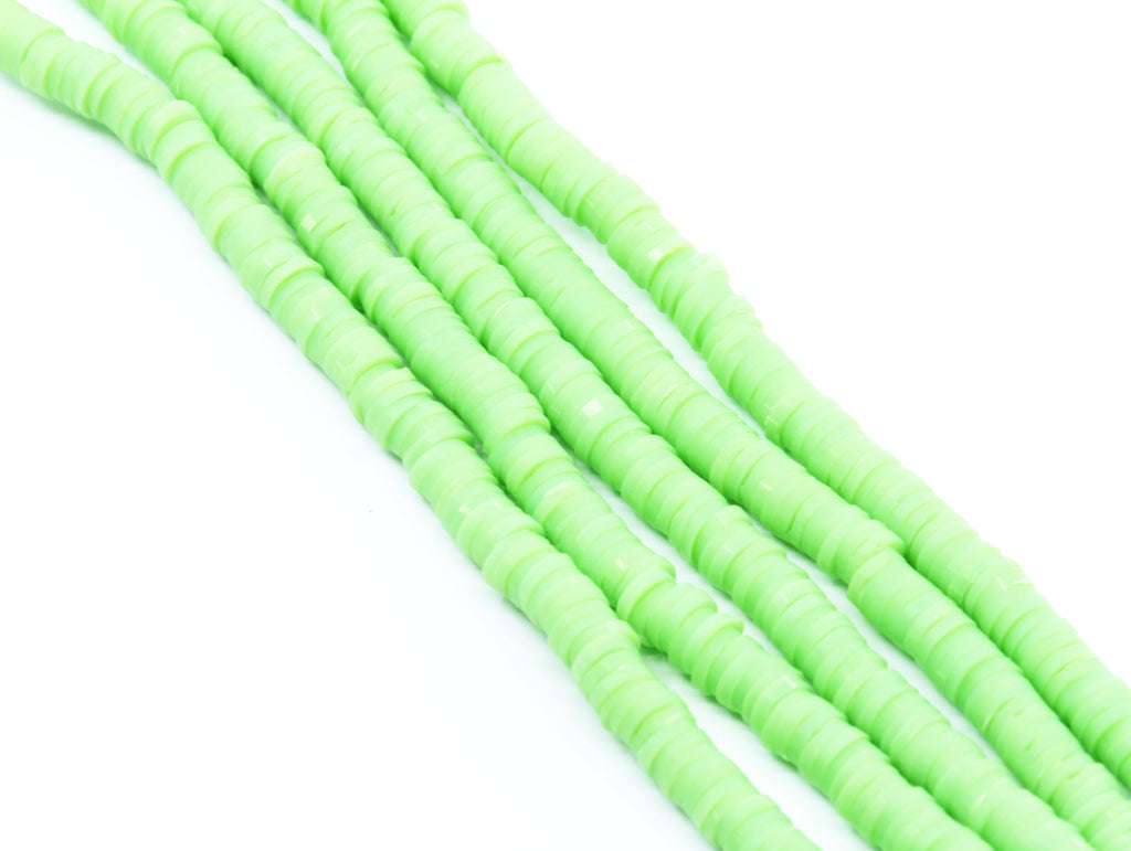 multiple strands of light green polymer clay disc beads  photographed diagonally on a clean white background.