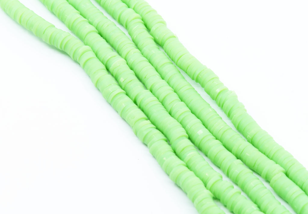 multiple strands of light green polymer clay disc beads  photographed diagonally on a clean white background.