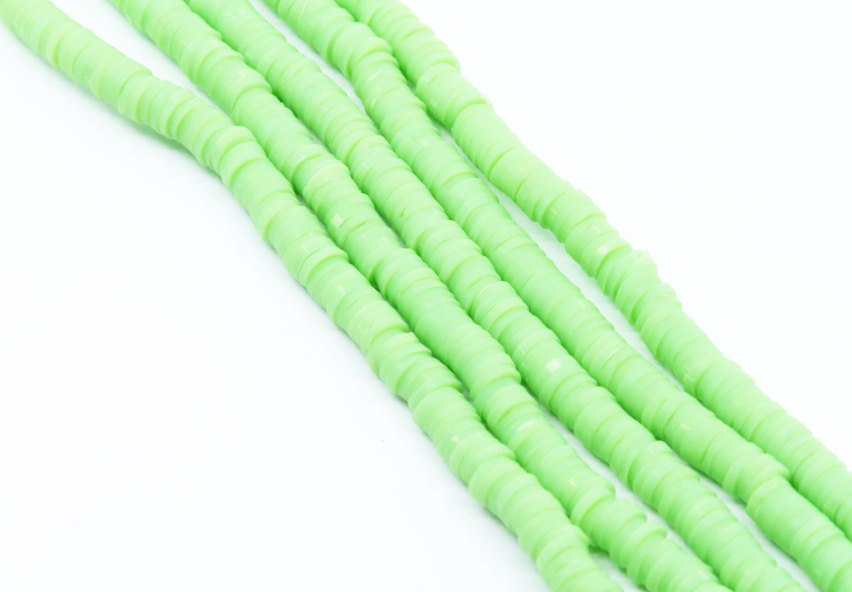 multiple strands of light green polymer clay disc beads  photographed diagonally on a clean white background.