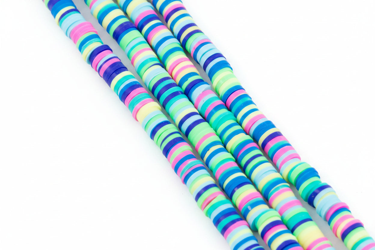 Four strands of multi-color blue, green and pink polymer clay beads on a white background.