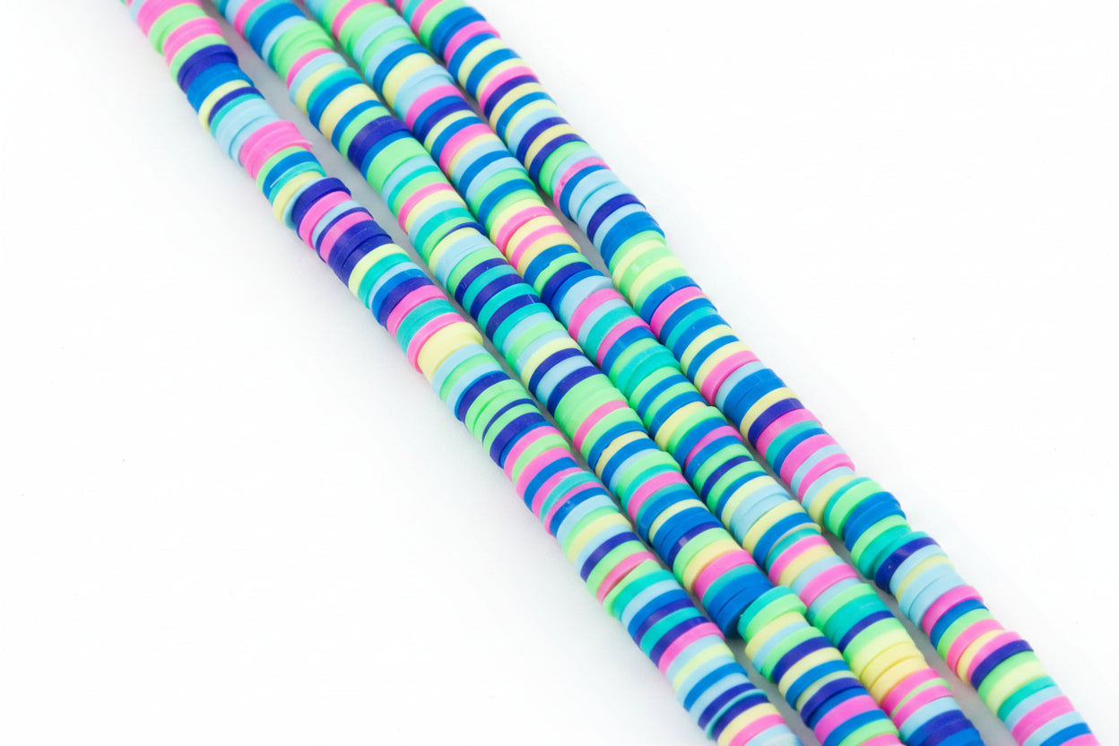 Four strands of multi-color blue, green and pink polymer clay beads on a white background.