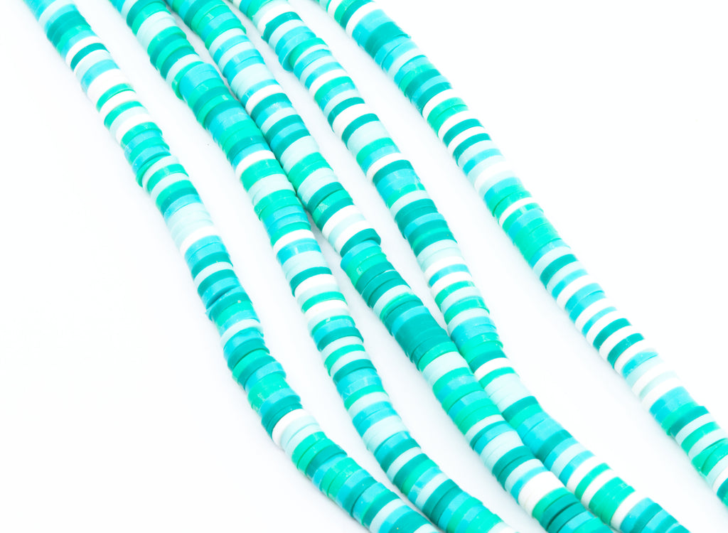 multiples strands of blue and green polymer clay disc beads arranged in diagonal strands on a white background.