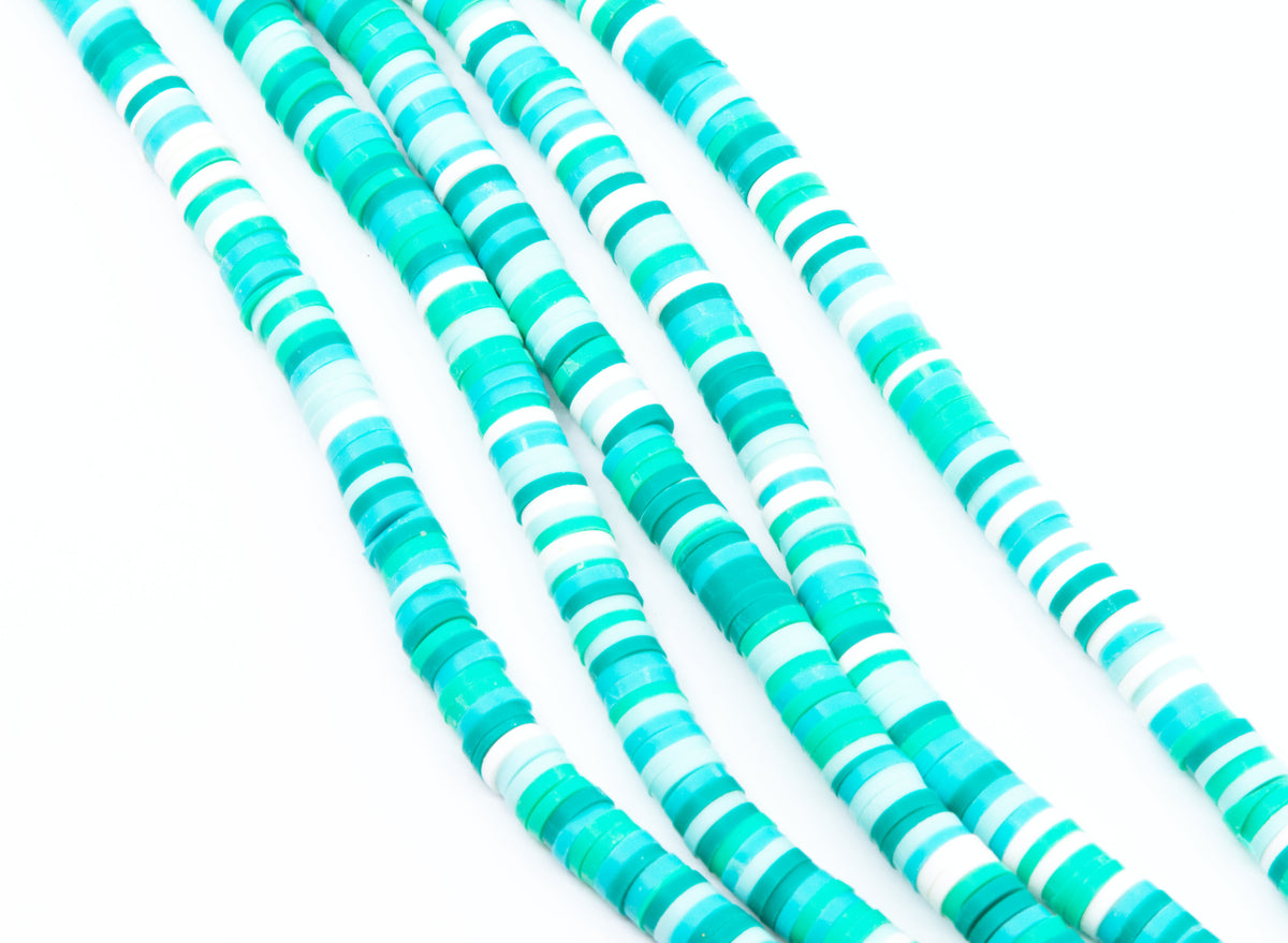 multiples strands of blue and green polymer clay disc beads arranged in diagonal strands on a white background.