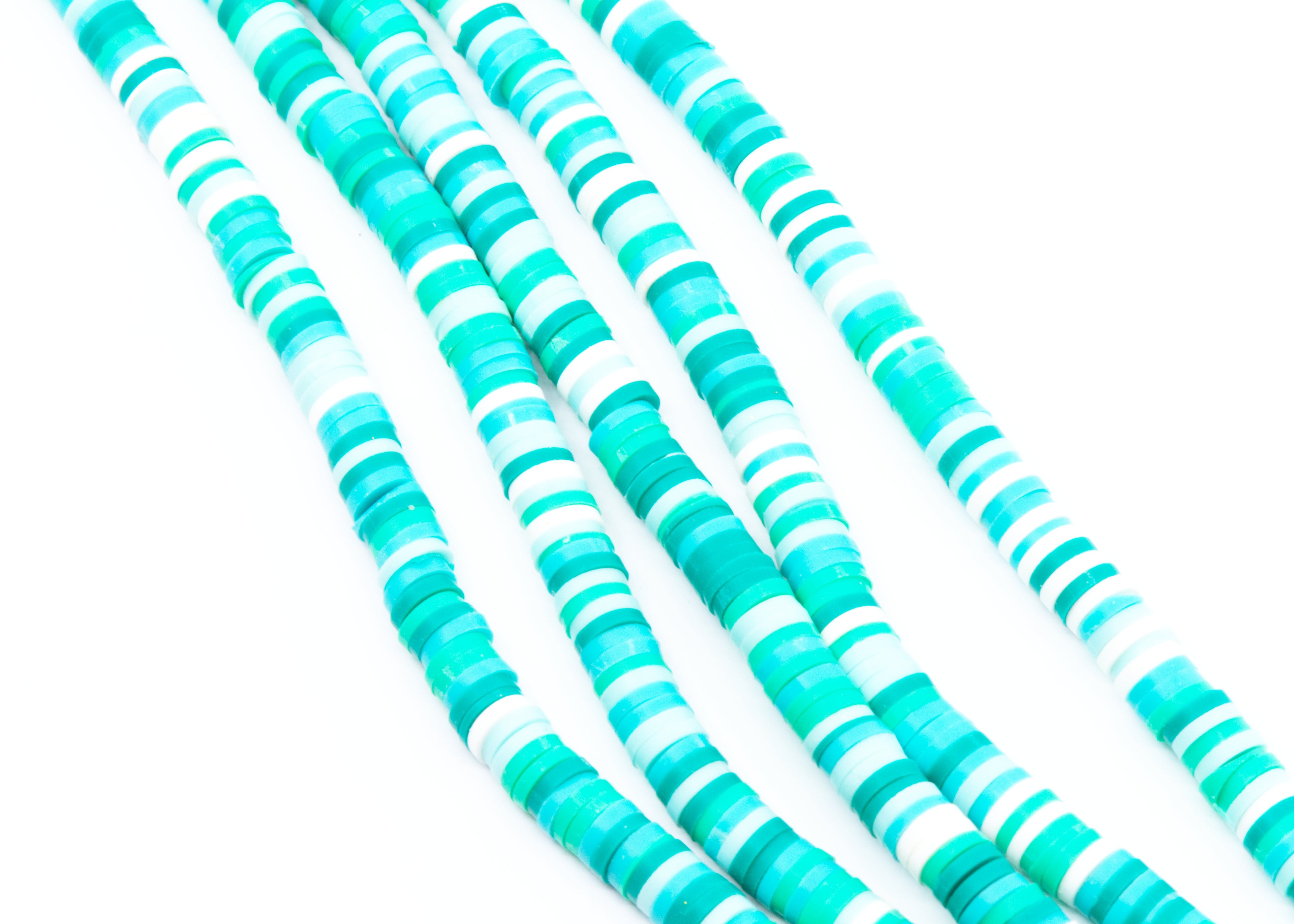 multiples strands of blue and green polymer clay disc beads arranged in diagonal strands on a white background.