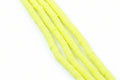 Four strands of bright neon yellow polymer clay disc beads arranged diagonally on a white background