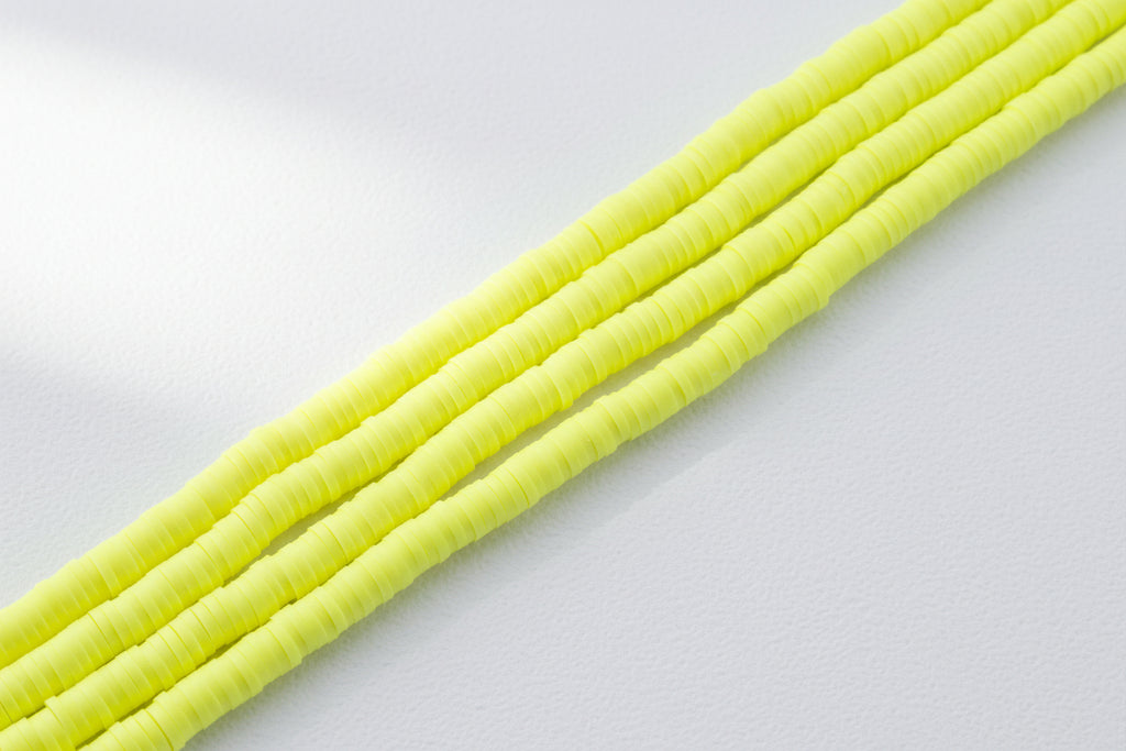 Four strands of bright neon yellow polymer clay disc beads arranged diagonally on a white background