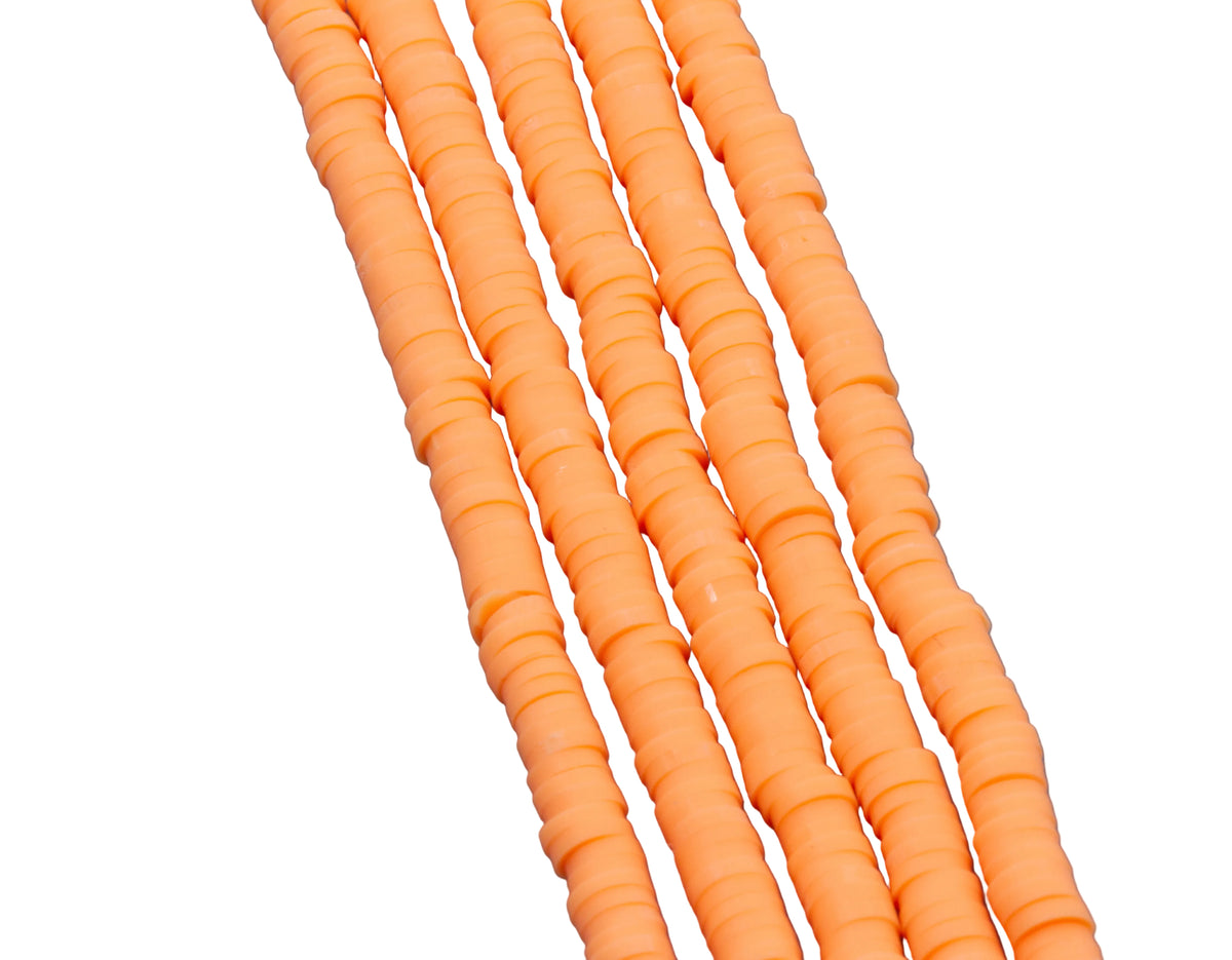 A close-up of several strands of orange polymer clay disc beads arranged diagonally on a white background.