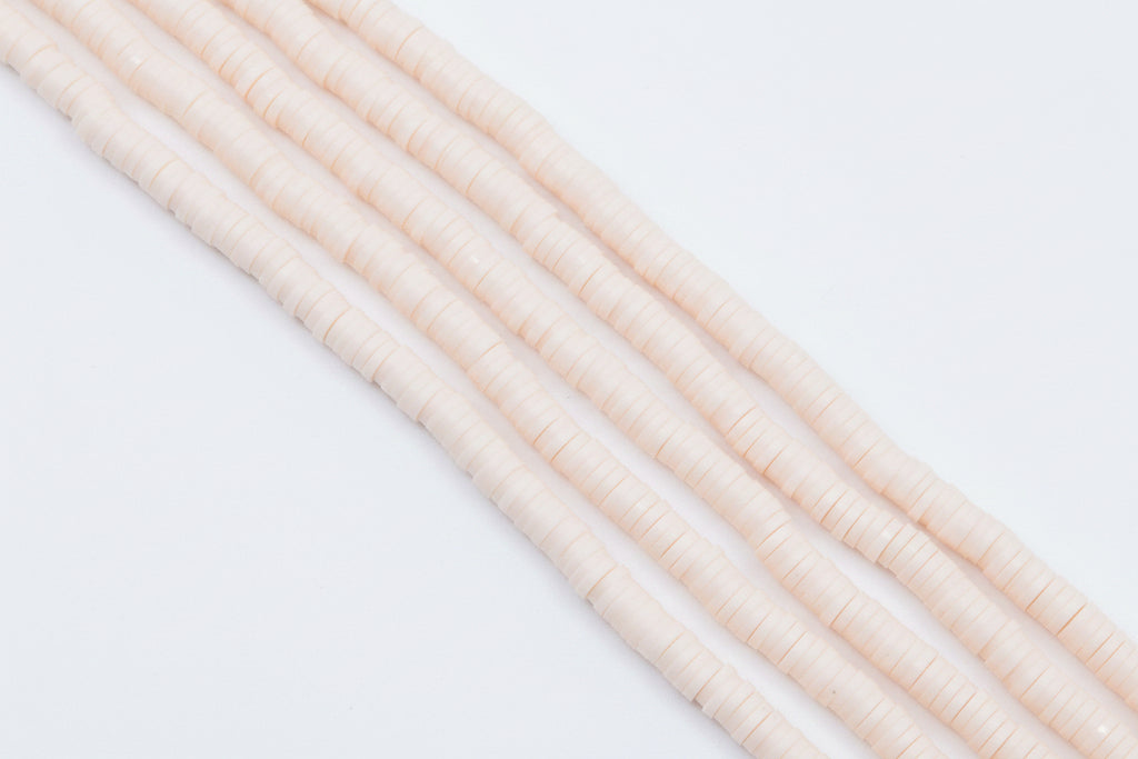 multiple strands of light peach colored polymer clay disc beads  arranged diagonally on a white background 