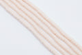 multiple strands of light peach colored polymer clay disc beads  arranged diagonally on a white background 