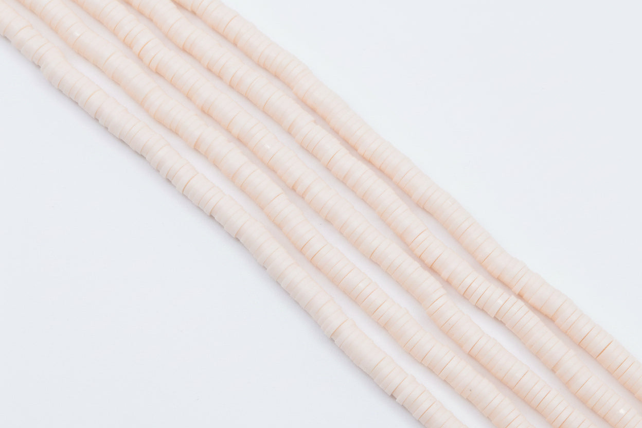 multiple strands of light peach colored polymer clay disc beads  arranged diagonally on a white background 
