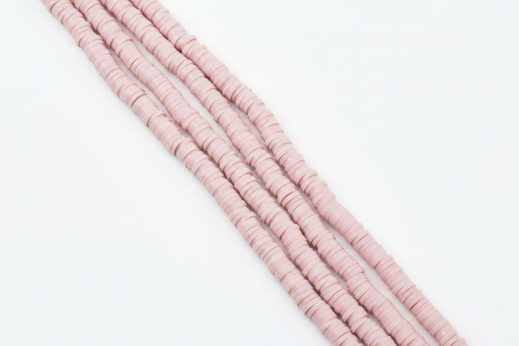 Four strands of pink polymer clay beads strands, arranged diagonally on a plain white background. 
