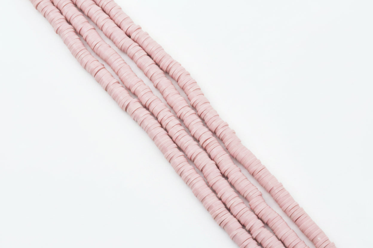 Four strands of pink polymer clay beads strands, arranged diagonally on a plain white background. 
