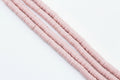 Four strands of pink polymer clay beads strands, arranged diagonally on a plain white background. 