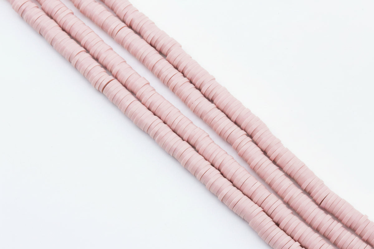 Four strands of pink polymer clay beads strands, arranged diagonally on a plain white background. 