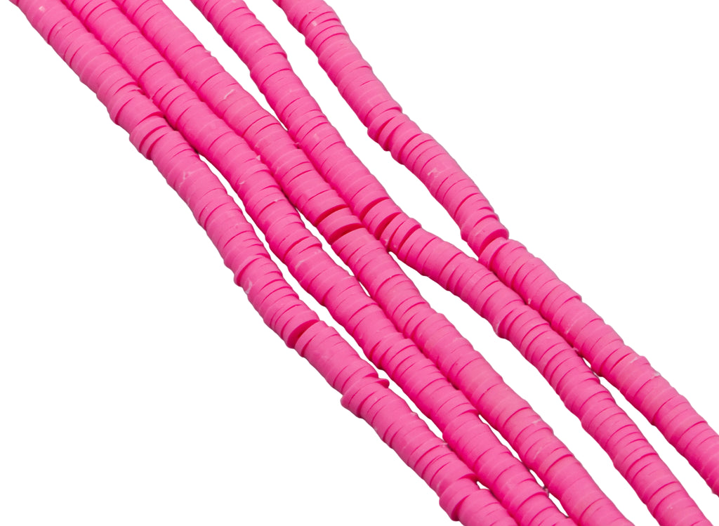 multiples strand of pink polymer clay disc beads photographed diagonally against a solid white background.