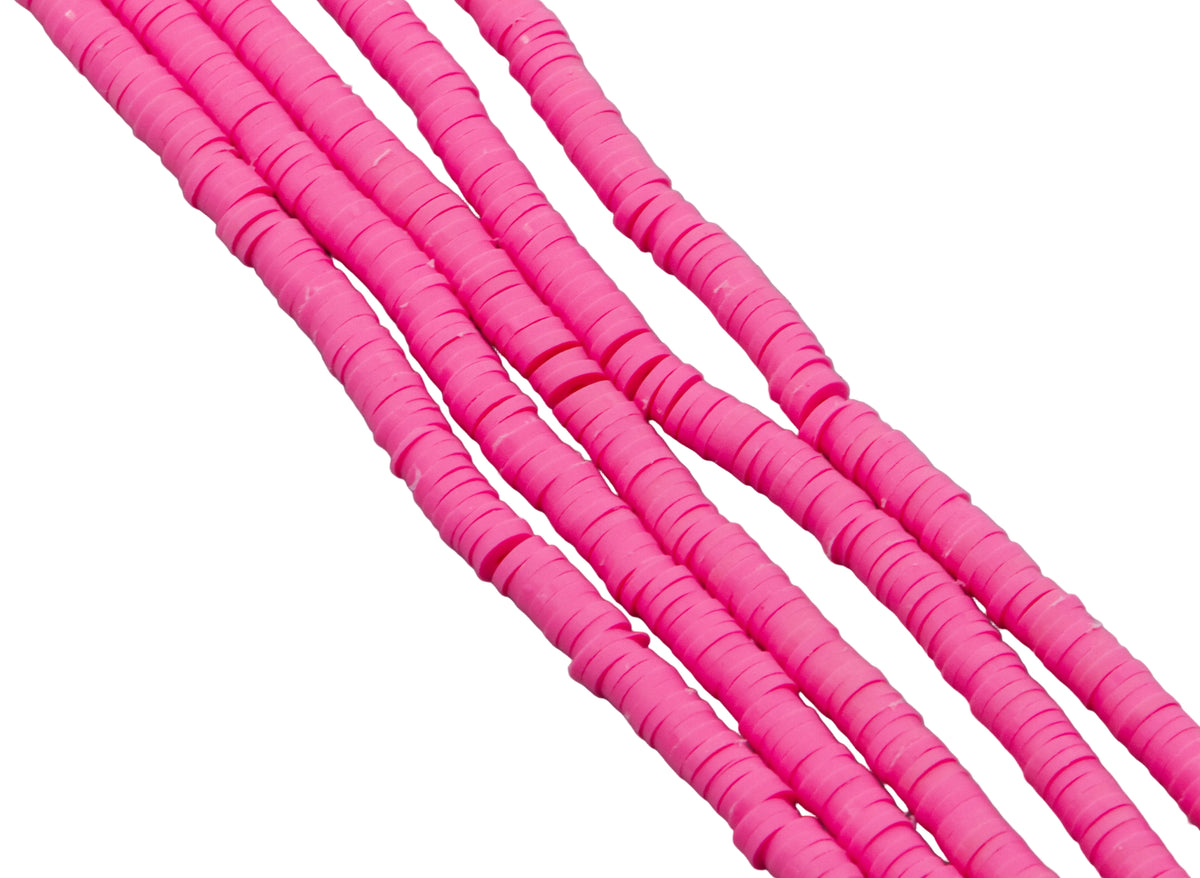 multiples strand of pink polymer clay disc beads photographed diagonally against a solid white background.