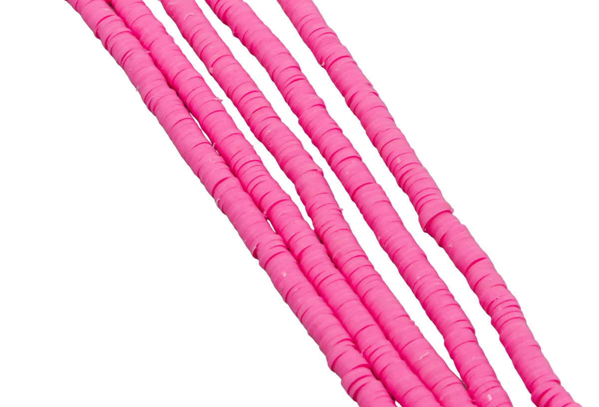 multiples strand of pink polymer clay disc beads photographed diagonally against a solid white background.