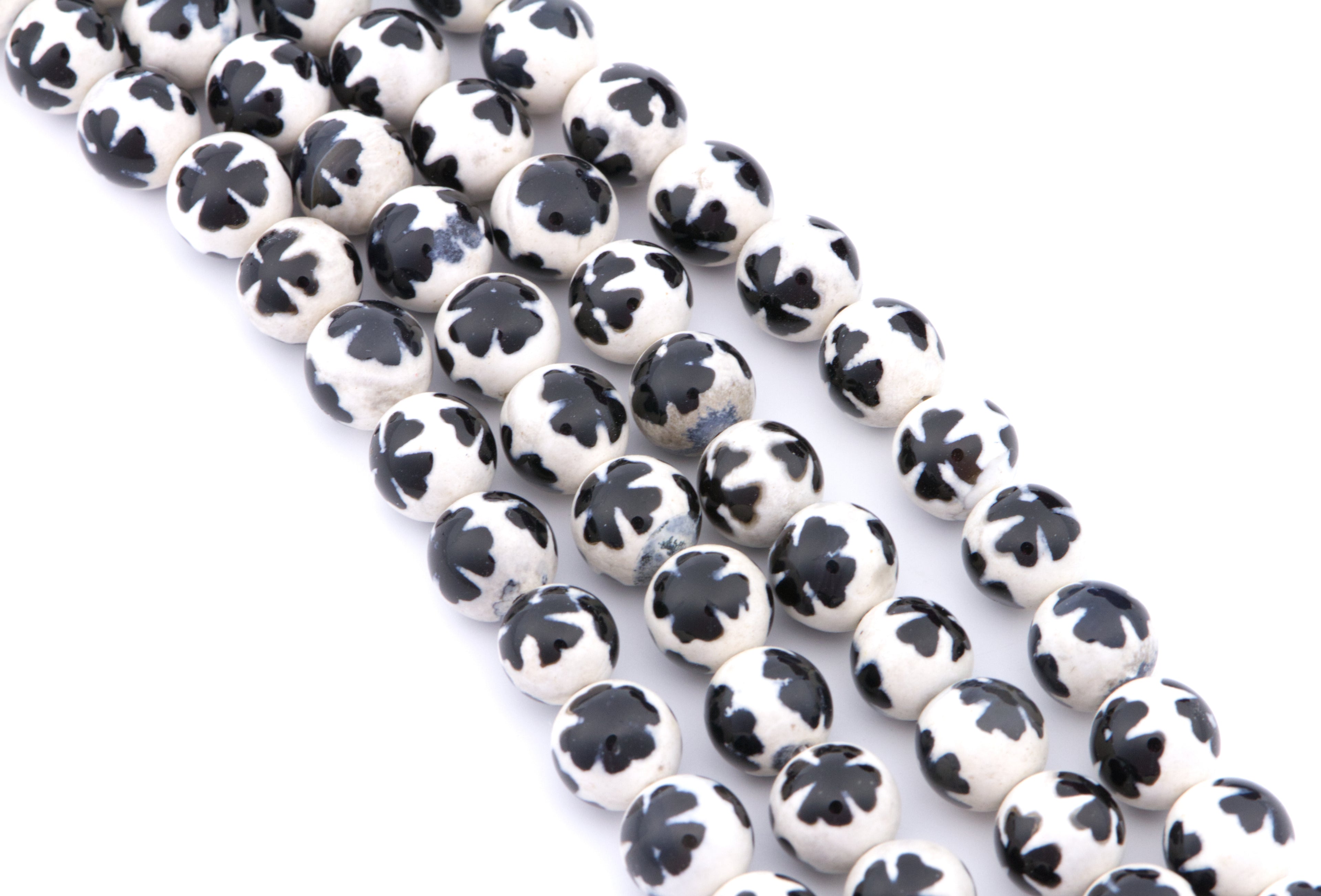Four strands of round white beads with a blue clover-like pattern, arranged diagonally on a white background.