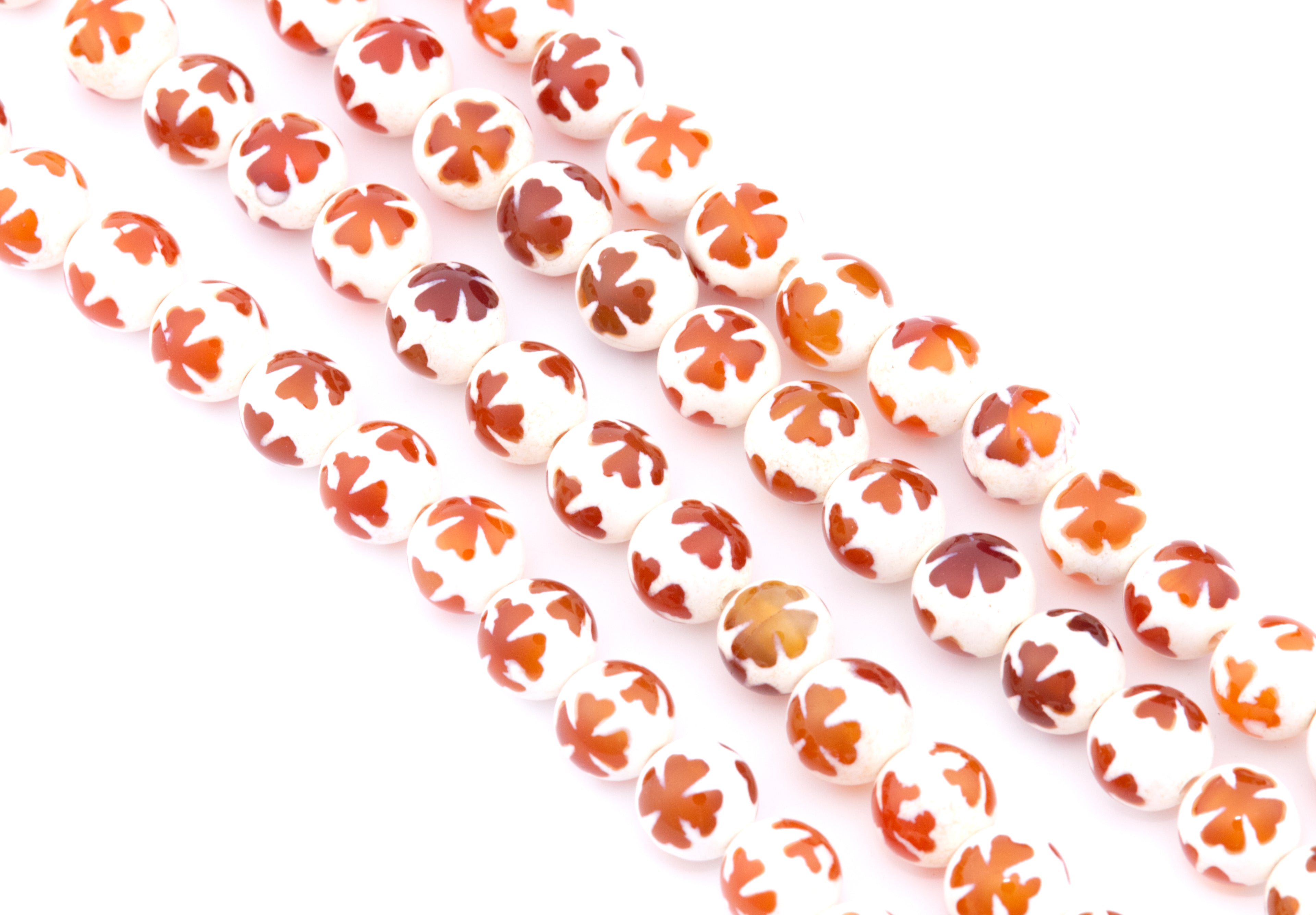 White round Tibetan agate beads with a white base and an orange clover design on top, arranged in diagonal strands on a white background.