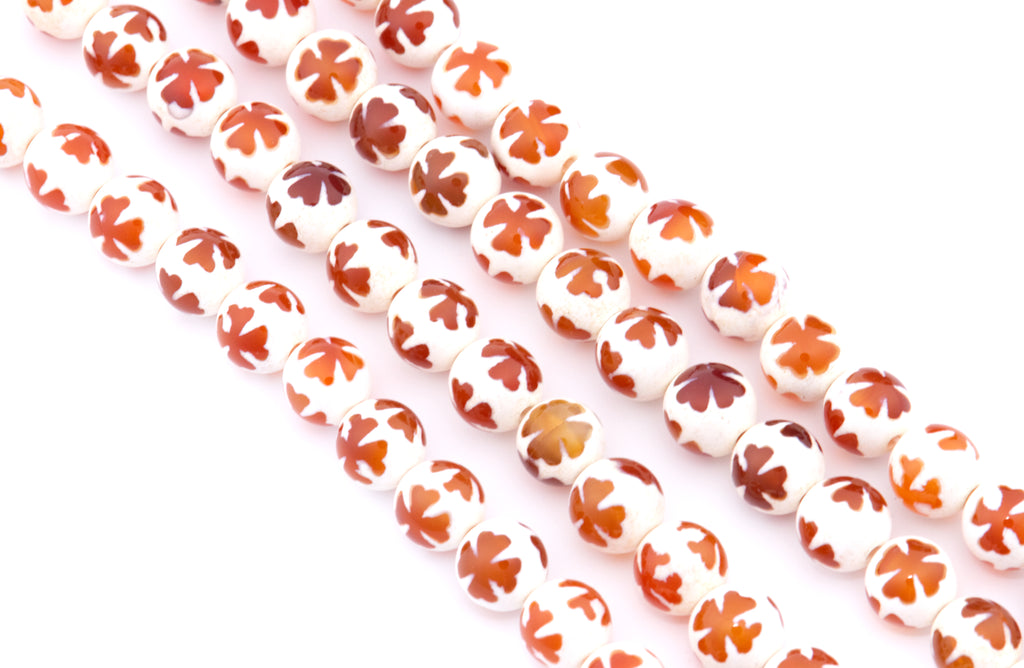 White round Tibetan agate beads with a white base and an orange clover design on top, arranged in diagonal strands on a white background.