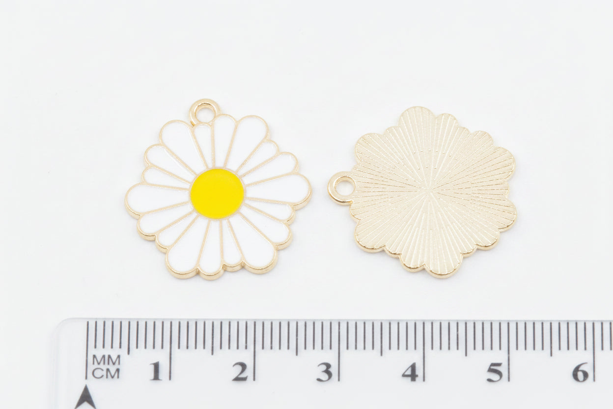 Two small flower-shaped jewelry charms on a white background, with a ruler at the bottom showing their size. One charm is a white daisy with a yellow center and gold-tone outline, and the other is the back view in a textured gold-tone finish.