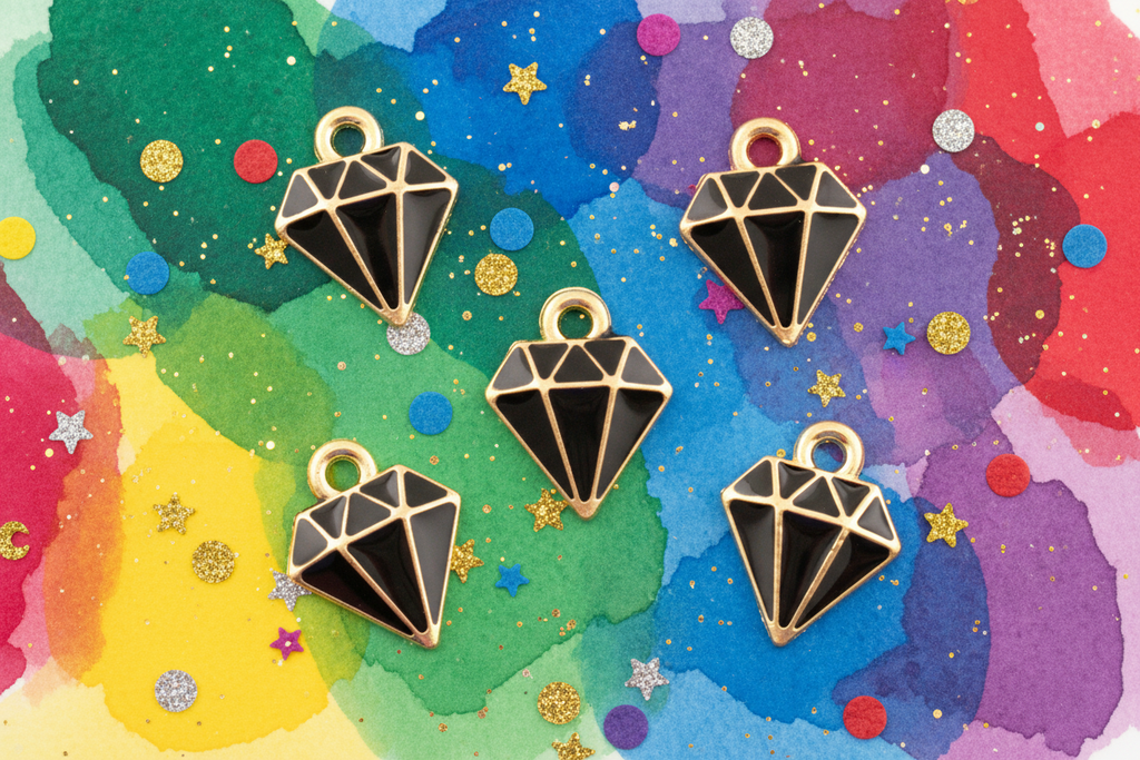Five black and gold diamond-shaped charms with hanging loops, arranged on a colorful watercolor background with glitter stars and confetti.