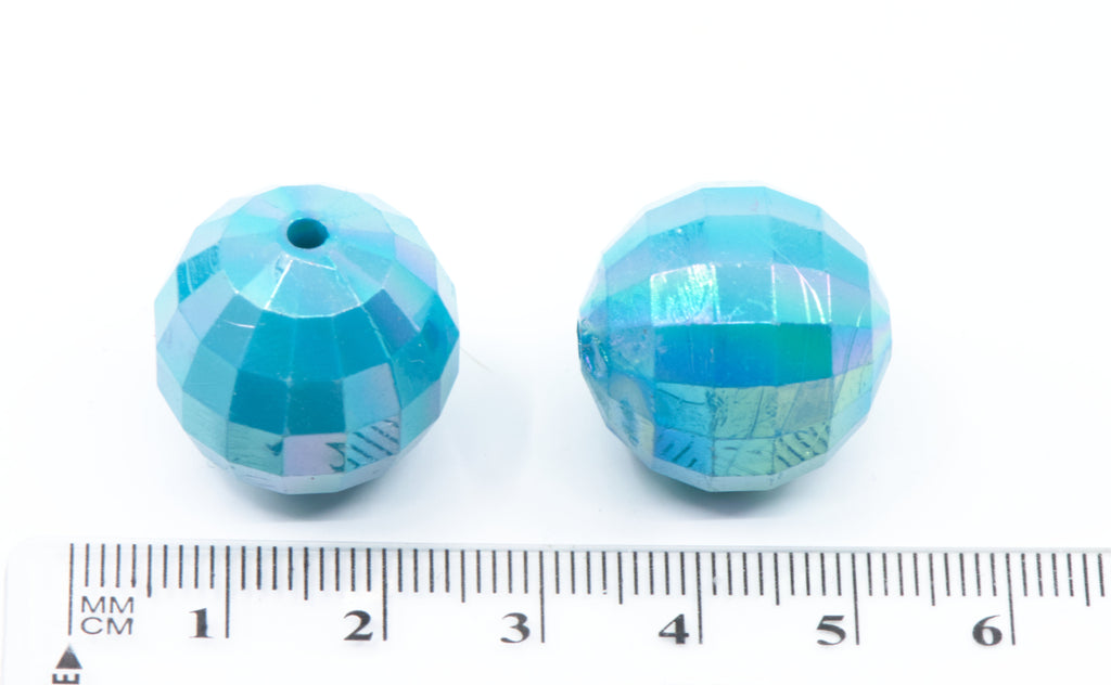 Two blue faceted beads with a ruler for scale on a white background